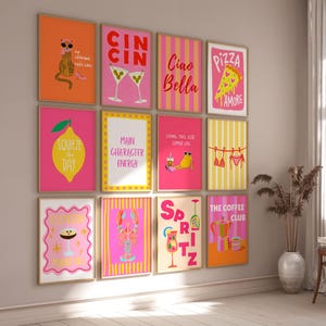 Op de afbeelding: Een verzameling ingelijste kunstprints met kleurrijke illustraties en tekst. De prints tonen verschillende thema's, waaronder cocktails, eten en inspirerende citaten. Het kleurenpalet omvat roze, oranje, geel en wit.