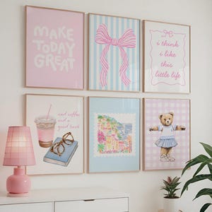 May include: A collection of framed art prints with a soft, pastel aesthetic. The prints feature various designs, including a pink bow on blue stripes, a teddy bear in a skirt, and the text "MAKE TODAY GREAT". A pink lamp sits on a white surface.