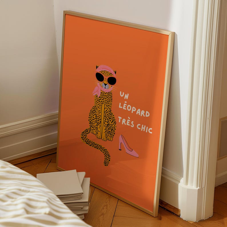 Op de afbeelding: Ingelijste kunstprint met een oranje achtergrond, met een cartoon luipaard met zonnebril, een roze sjaal en een hoofdband. Er staat een roze high heel schoen naast het luipaard. De Franse tekst "UN L&Eacute;OPARD TR&Egrave;S CHIC" staat ook op de print.