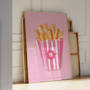 May include: A pink and white striped container filled with watercolor-style french fries. The fries are shades of orange and yellow. The artwork is framed in gold and set against a pink background. The container has a pink logo with a silhouette of a woman's head.
