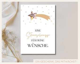 May include: A white card with a gold star and a gold shooting star with the text "Eine Sterneschnuppe für deine Wünsche. Ein Geschenk, das mitwächst!"