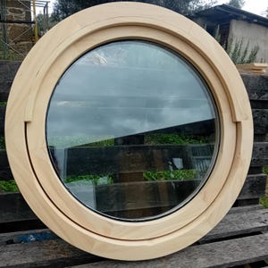 May include: A round wooden window frame with a clear glass pane. The frame is made of light wood and has a simple design.