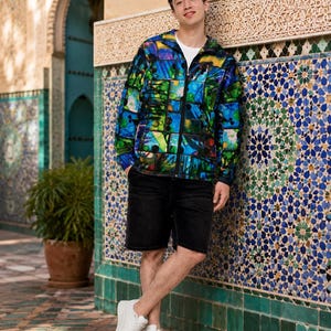 May include: A long-sleeve zip-up jacket featuring a vibrant, multi-colored abstract print in shades of blue, green, and yellow, worn over a plain white t-shirt with black denim shorts and clean white athletic sneakers.