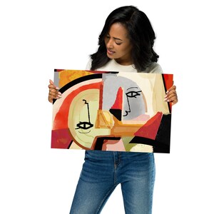 K&ouml;nnte beinhalten: Abstrakter Kunstdruck mit einem geometrischen Design und Gesichtern in Rot, Gelb, Grau und Schwarz. Das Kunstwerk wird von einer Person gehalten.