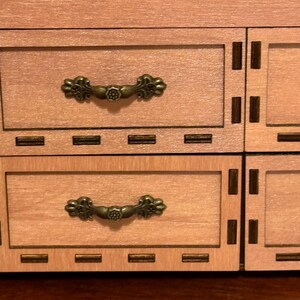 May include: A wooden jewelry box with two drawers and ornate metal handles. The box has a light brown finish and a decorative border around the drawers.