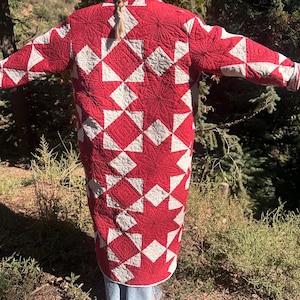 May include: A long-sleeved coat crafted from a red and white quilted fabric featuring a repeating geometric star pattern. The garment displays intricate stitching throughout the surface, creating a textured appearance across the back and sleeves.