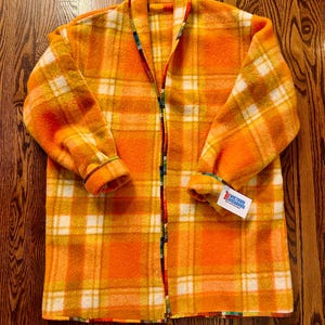 May include: Orange and yellow plaid jacket with a full-length zipper. The jacket has a colorful patterned lining and cuffs. A tag is attached to the sleeve. The jacket is made of a thick, warm material.