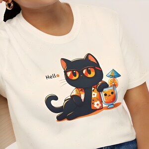 Può includere: T-shirt color crema con un gatto nero dei cartoni animati con occhiali da sole e una camicia hawaiana, che tiene in mano un cocktail con un ombrellino. La parola "Hello" è stampata sulla maglietta.