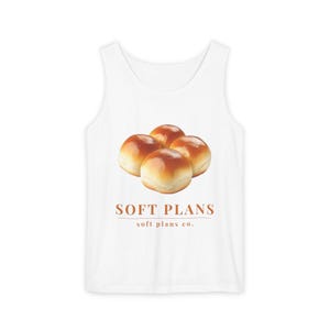 May include: A white tank top featuring a graphic of four golden-brown dinner rolls centered on the chest. Below the rolls, the text reads "SOFT PLANS" in large orange letters, with "soft plans co." in smaller orange text underneath.