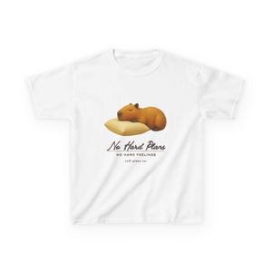 May include: A white t-shirt featuring a graphic of a brown capybara sleeping on a beige pillow. Below the illustration, the text reads "No Hard Plans", "NO HARD FEELINGS", and "soft plans co." in a dark, stylized font centered on the chest.