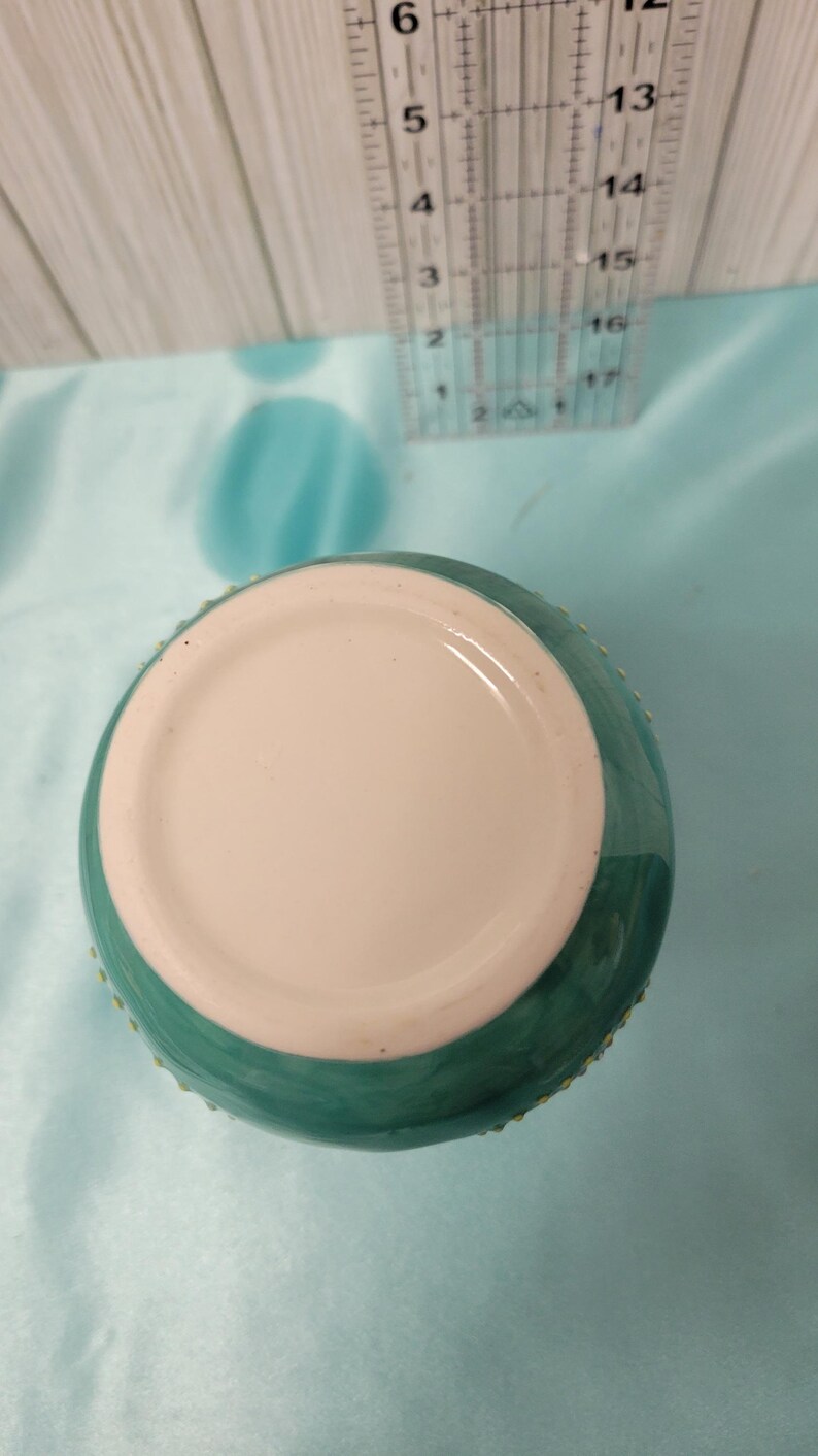 K&ouml;nnte beinhalten: Eine t&uuml;rkisfarbene Keramikvase mit wei&szlig;em Innenraum. Die Vase hat eine abgerundete Form und eine strukturierte Au&szlig;enseite. Ein transparentes Lineal befindet sich im Hintergrund, mit Messungen in Zentimetern.