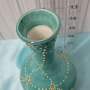 K&ouml;nnte beinhalten: Eine t&uuml;rkisfarbene Keramikvase mit rundem K&ouml;rper und ausgestellter &Ouml;ffnung. Die Vase ist mit einem Muster aus kleinen gelben und orangefarbenen Punkten verziert. Das Innere der Vase ist wei&szlig;. Ein Lineal ist im Hintergrund zu sehen.