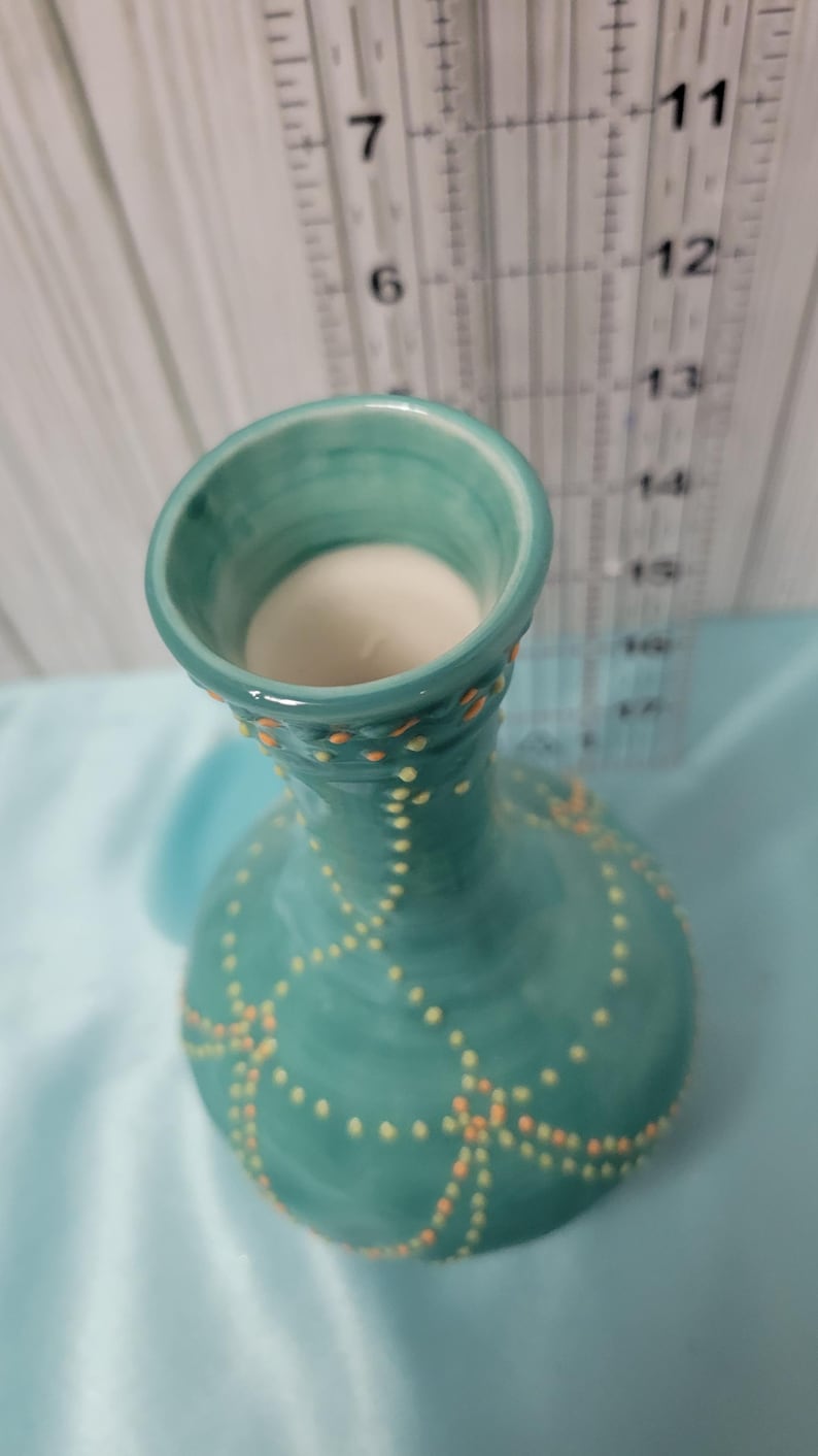 K&ouml;nnte beinhalten: Eine t&uuml;rkisfarbene Keramikvase mit rundem K&ouml;rper und ausgestellter &Ouml;ffnung. Die Vase ist mit einem Muster aus kleinen gelben und orangefarbenen Punkten verziert. Das Innere der Vase ist wei&szlig;. Ein Lineal ist im Hintergrund zu sehen.