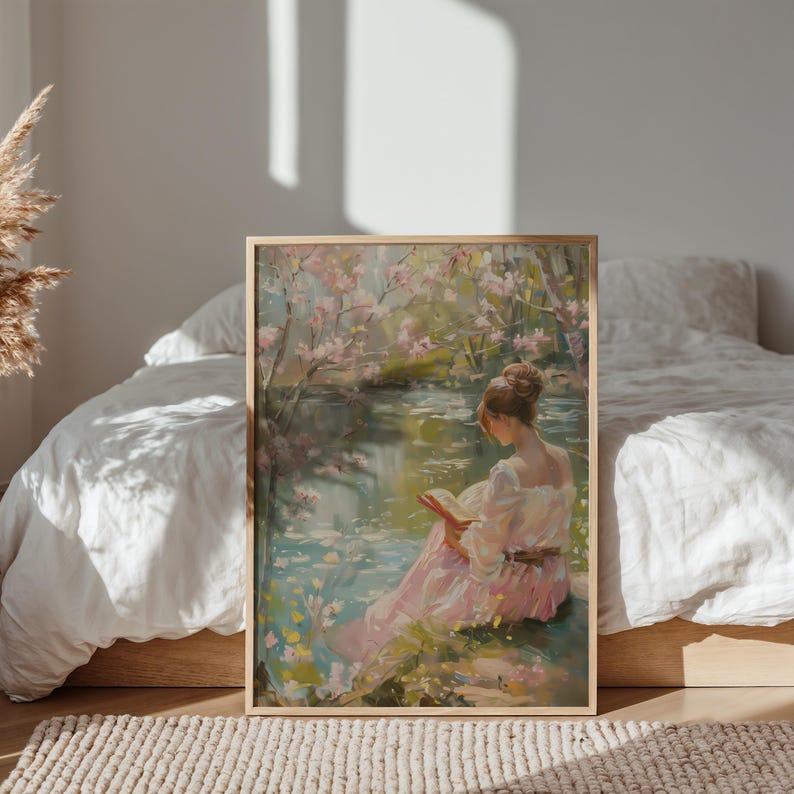 May include: A framed art print depicts a woman reading by a tranquil lake. The artwork features soft pastel colors, with pink blossoms and a woman in a pink dress. The scene is set in a serene outdoor environment, evoking a sense of peace and contemplation.