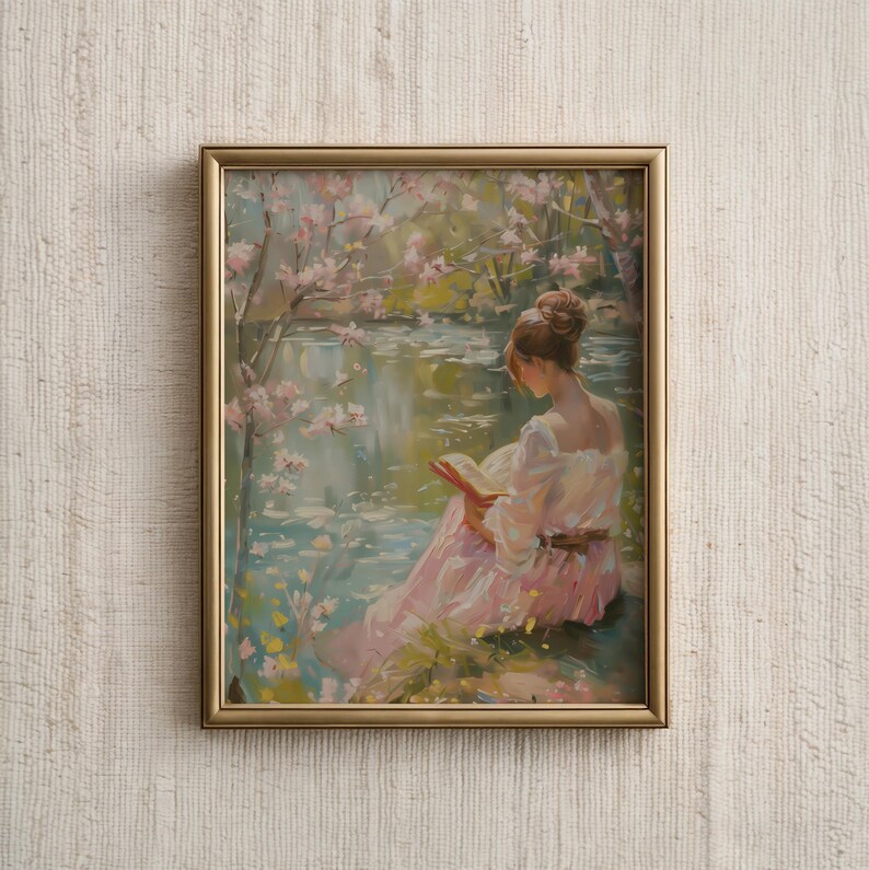 May include: Framed artwork depicting a woman reading by a lake. The painting features soft colors, with a woman in a pink dress, a gold frame, and a serene waterscape with blossoming trees. The artwork evokes a sense of tranquility.