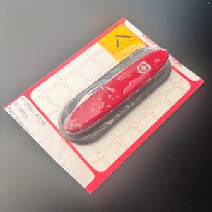 Puede incluir: Una navaja suiza roja con un emblema de cruz blanca, empaquetada en una tarjeta roja y blanca. El embalaje incluye el texto "Victorinox" y "Swiss Collection". La navaja está en un envoltorio de plástico transparente.