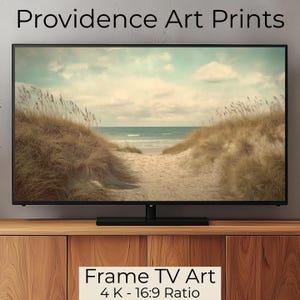 May include: A framed TV art print featuring a beach scene with a path leading through sand dunes to the ocean. The sky is a soft blue with white clouds. The print is in a 4K - 16:9 ratio. Frame TV Art.