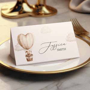 Op de afbeelding: Een naambordje met een gouden rand, met een aquarel illustratie van een teddybeer in een luchtballon. De kaart heeft de naam "Jessica Smith" in elegant schrift. De ballon is hartvormig.