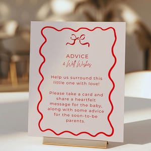 May include: A white sign with red decorative border and text that reads "ADVICE & Well Wishes". The sign is held by a gold metal stand. The text encourages guests to share advice and well wishes for the baby and parents.