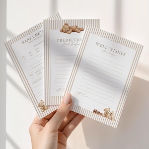 May include: Three baby shower prediction and well-wish cards. The cards have a striped beige and white background with teddy bear illustrations. Text on the cards includes "Baby Laws", "Predictions", and "Well Wishes".