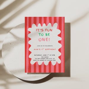 Op de afbeelding: Een kleurrijke verjaardagsuitnodiging met een rood-roze gestreepte achtergrond. De uitnodiging bevat de tekst "IT'S FUN TO BE ONE!" in een witte, golvende vorm. Extra tekst bevat de verjaardagsdetails.