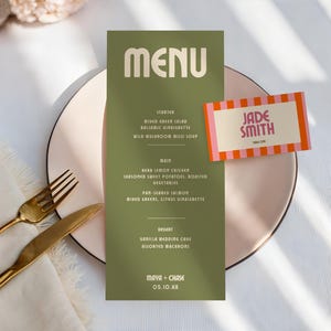 Op de afbeelding: Een trouwmenu en een naamkaartje. Het menu is olijfgroen met witte tekst en bevat voorgerechten, hoofdgerechten en desserts. Een naamkaartje met roze en oranje strepen en de naam "Jade Smith" ligt op een roze bord met gouden bestek.