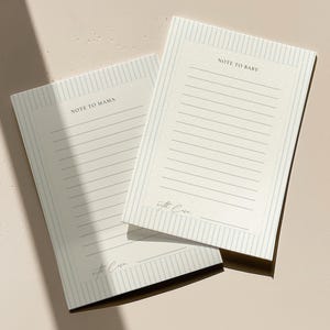 May include: Two cream-colored notepads with lined pages and vertical striped borders. One notepad reads "NOTE TO MAMA" and the other reads "NOTE TO BABY". Both notepads have the text "with love" at the bottom.