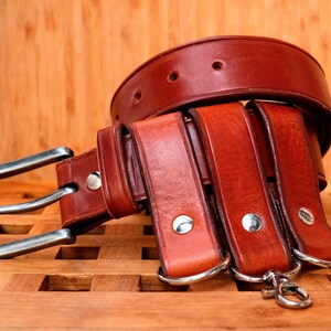 May include: A brown leather belt with multiple layers and a silver buckle. The belt is on a wooden surface.