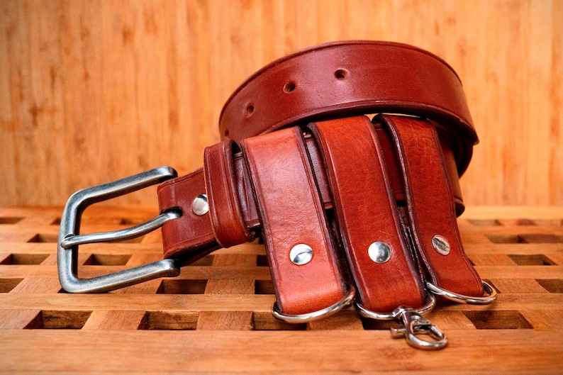 May include: A brown leather belt with multiple layers and a silver buckle. The belt is on a wooden surface.
