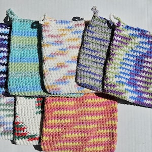 May include: A collection of seven handmade crochet potholders in various colors. The potholders feature a loop for hanging and are in shades of purple, blue, green, yellow, and white. The crochet stitch creates a textured surface.
