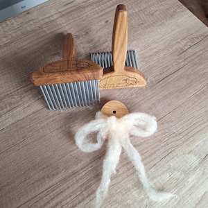 May include: Two wooden wool combs with metal tines and a wooden handle, along with a small piece of white wool. The combs have the text "Woolly lamb" engraved on them. The items are arranged on a wooden surface.