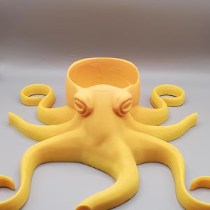 May include: A yellow octopus-shaped planter with a round opening at the top. The planter is made of plastic and has a smooth, matte finish.