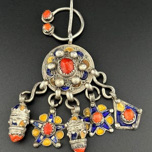 May include: A silver pendant with a circular design and multiple dangling charms. The pendant is decorated with blue and yellow enamel and red coral stones.