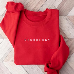 Puede incluir: Sudadera roja con la palabra "NEUROLOGY" impresa en blanco en la parte delantera.