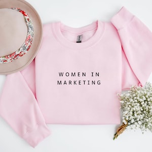 May include: Pink sweatshirt with the text "Women in Marketing" printed in black.