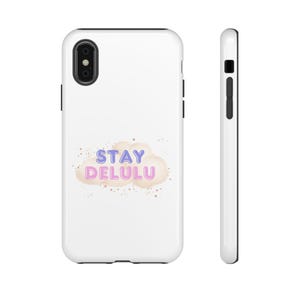 Peut inclure: Coque de téléphone blanche avec le texte "STAY DELULU" en lettres violettes et roses, avec un motif de nuage. L'étui a un objectif d'appareil photo noir et des boutons latéraux noirs.