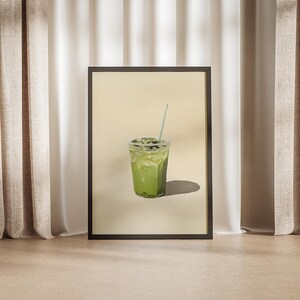 May include: A framed print of a green iced drink with a straw in a clear plastic cup. The drink is on a light beige background.