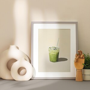 May include: A framed print of a green iced drink with a straw in a clear plastic cup. The print is on a beige background and is framed in a light gray frame.