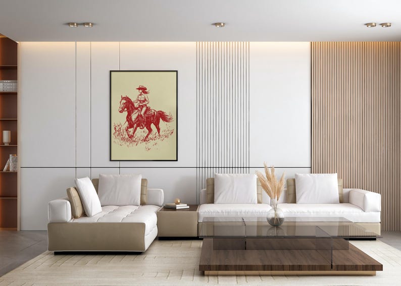 May include: Framed art print featuring a red illustration of a person riding a horse. The artwork is set against a cream-colored background and framed in black. The image is displayed in a modern living room setting.