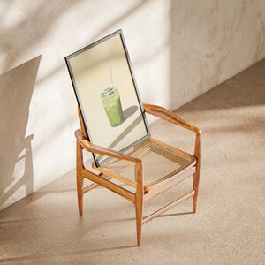 May include: A framed print of a green iced drink with a straw, sitting on a wooden chair with a woven cane seat.