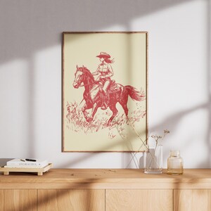Vintage red line illustration of a cowgirl riding a galloping horse through grass, set on a cream background in rustic Western style.