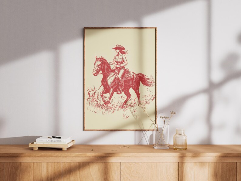Vintage red line illustration of a cowgirl riding a galloping horse through grass, set on a cream background in rustic Western style.