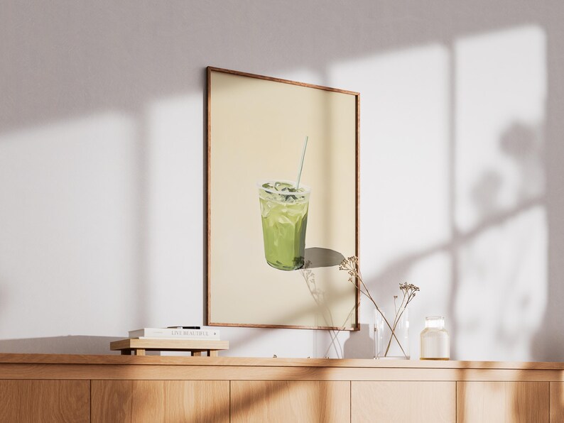 May include: A framed print of a green iced drink with a straw in a clear plastic cup. The background is a light yellow color.