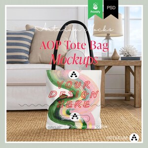 Könnte beinhalten: Eine weiße Tragetasche mit schwarzem Griff und einem farbenfrohen abstrakten Design mit dem Text "YOUR DESIGN HERE". Die Tasche wird in einer Mockup-Umgebung mit Sofa, Kissen und einem Holztisch präsentiert. Die Worte "AOP Tote Bag Mockups" sind ebenfalls sichtbar.