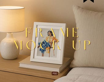 May include: A white framed picture featuring a person in colourful clothing, resting on books. The words "FRAME MOCK UP" are overlaid. A lamp and pillow are in the background. The image is a mockup.