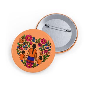 Peut inclure: Deux boutons ronds orange. L'un présente un motif de cœur floral avec une mère et deux enfants. L'autre bouton est argenté avec une épingle au dos. Le motif comprend des fleurs roses, bleues et oranges.