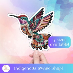 Może przedstawiać: Kolorowa naklejka z kolibrym z misternymi wzorami z koralików w odcieniach czerwieni, pomarańczy, żółci, zieleni, błękitu i fioletu. Naklejka znajduje się na białym tle i jest trzymana przez rękę. Tekst "Dostępne 3 rozmiary!" znajduje się w białym polu z niebieską ramką. Tekst "Sklep należący do rdzennych mieszkańców!" znajduje się w niebieskim polu z białą ramką.