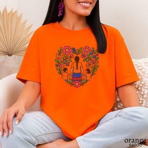 May include: Bright orange t-shirt featuring a heart-shaped floral design with a mother and two children holding hands. The graphic includes pink, blue, and yellow flowers. The text "orange 64000" is printed at the bottom.