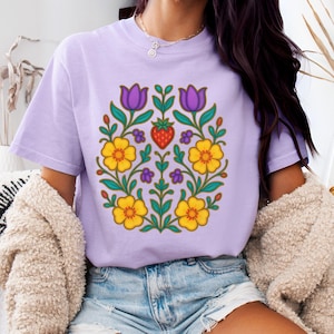 May include: A light purple t-shirt featuring a floral design with yellow flowers, purple tulips, and a red strawberry at the center. The design is surrounded by green leaves and stems. The shirt is made of a soft material.