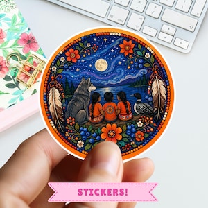 Può includere: Un adesivo circolare raffigurante una scena notturna con luna piena, un lupo, un strolaga e tre bambini seduti vicino a un lago. Il design è incorniciato da bordi arancioni, piume e motivi floreali con bacche blu in uno stile vivace.